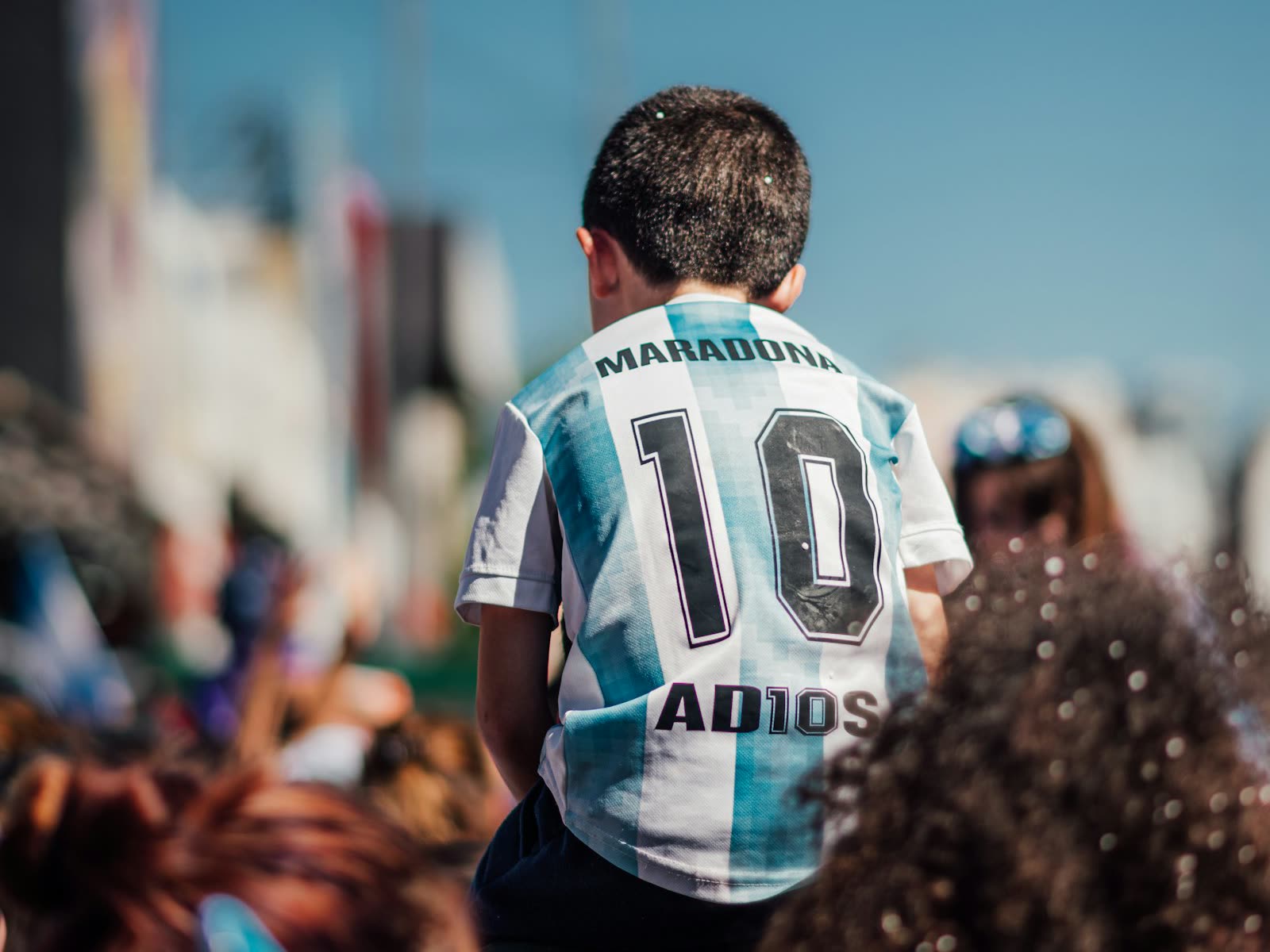 Un nene con la camiseta 10 de Maradona, subido a los hombros de un adulto en la tribuna